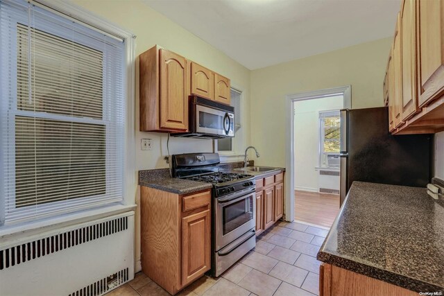 85-10 34th Ave Unit 421, Jackson Heights, NY 11372 - kitchen with stainless steel appliances, radiator, dark countertops, a sink, and light tile patterned floors