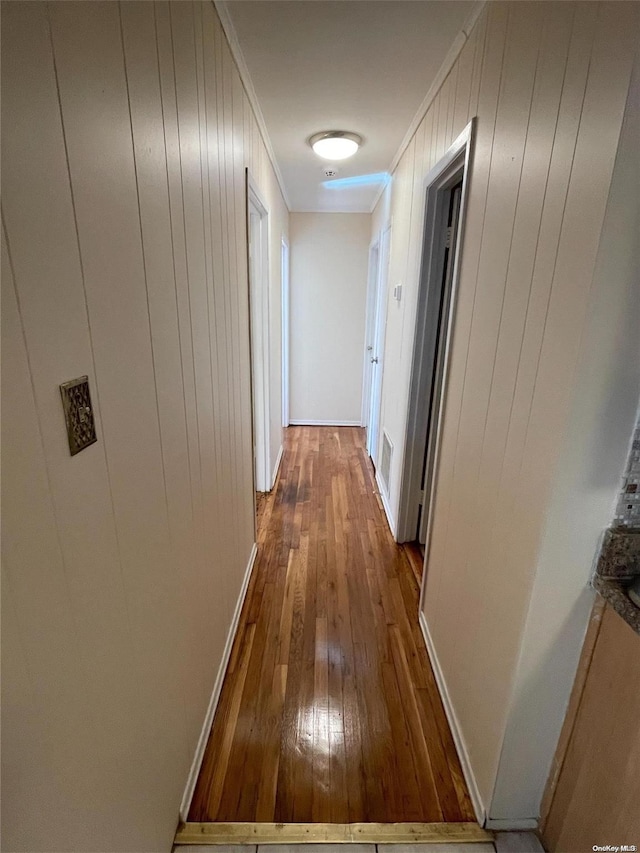 hall with wood walls, wood-type flooring, and crown molding