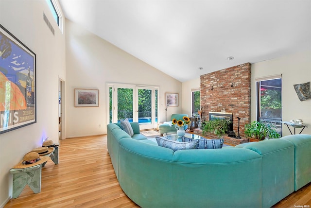 living room featuring high vaulted ceiling, light hardwood / wood-style floors, and a brick fireplace