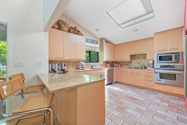 kitchen featuring kitchen peninsula, light brown cabinetry, a kitchen breakfast bar, stainless steel appliances, and vaulted ceiling