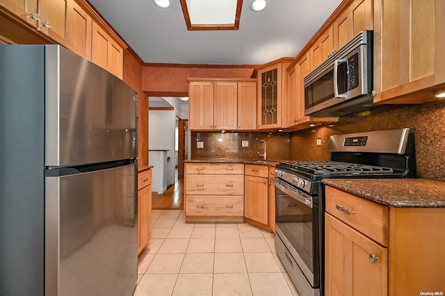 kitchen with sink, decorative backsplash, dark stone countertops, light tile patterned floors, and stainless steel appliances