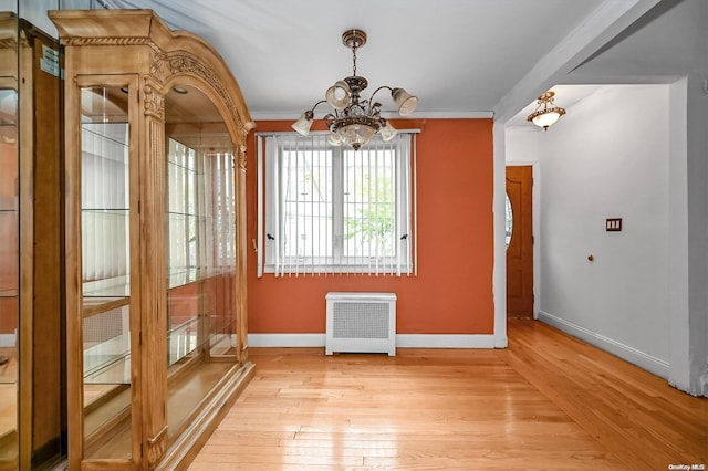 unfurnished dining area featuring radiator, crown molding, light hardwood / wood-style floors, and an inviting chandelier