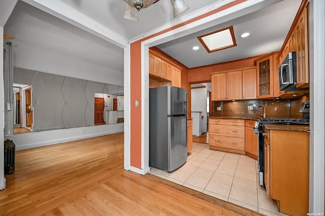 kitchen featuring dark stone countertops, decorative backsplash, light hardwood / wood-style flooring, and appliances with stainless steel finishes