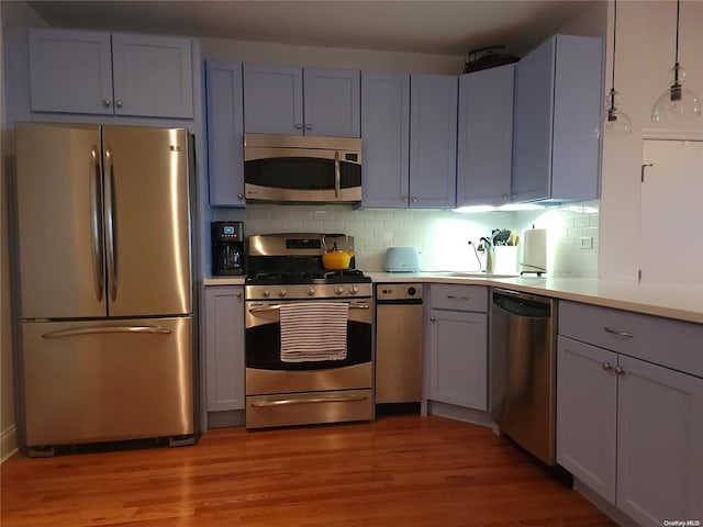 kitchen with backsplash, stainless steel appliances, hanging light fixtures, and light hardwood / wood-style flooring