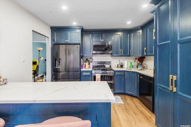 kitchen featuring sink, stainless steel appliances, blue cabinets, light hardwood / wood-style floors, and a breakfast bar