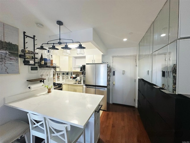 kitchen with kitchen peninsula, dark hardwood / wood-style floors, decorative light fixtures, stainless steel refrigerator, and white cabinets