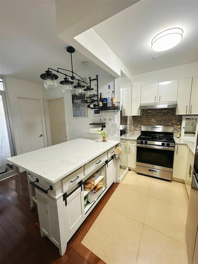 kitchen featuring hanging light fixtures, white cabinets, decorative backsplash, and stainless steel gas stove