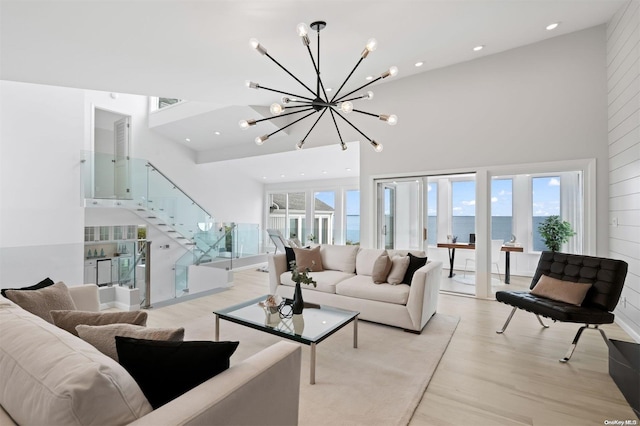 living room with a high ceiling, a water view, light hardwood / wood-style floors, and a notable chandelier