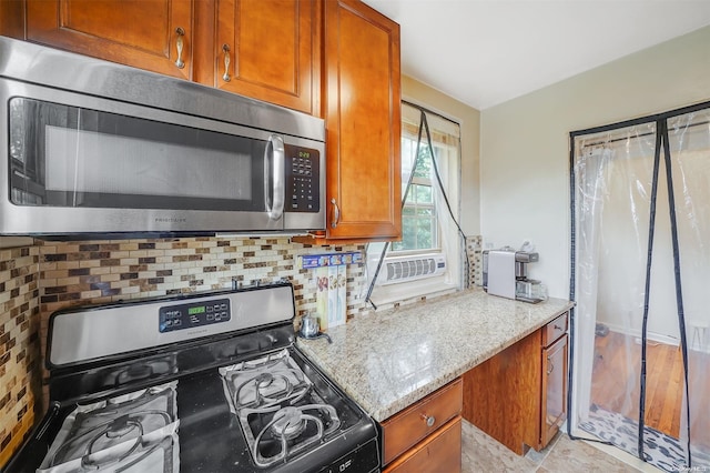 kitchen featuring gas range oven, light wood-type flooring, backsplash, and light stone counters