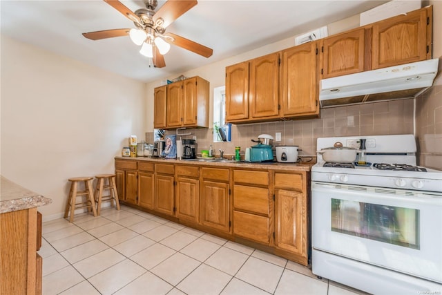 kitchen with white range with gas stovetop, light tile patterned floors, tasteful backsplash, and ceiling fan