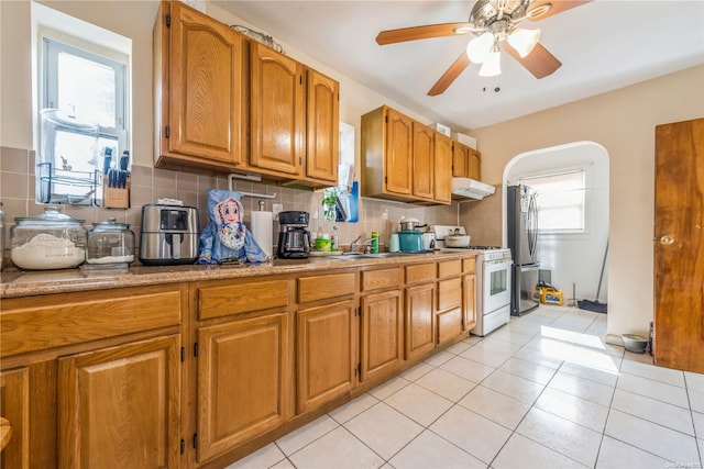 kitchen featuring stainless steel fridge, white gas range oven, light tile patterned floors, and a healthy amount of sunlight