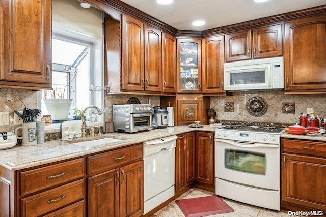 kitchen featuring decorative backsplash, light stone counters, sink, and white appliances