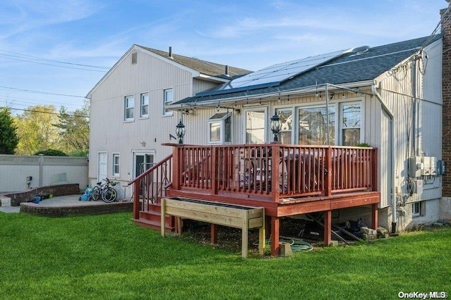 back of property featuring a lawn, a wooden deck, and solar panels