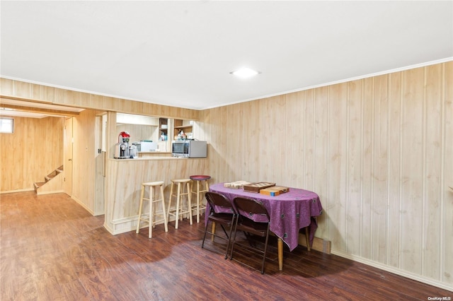 dining space with bar area, dark hardwood / wood-style flooring, crown molding, and wood walls