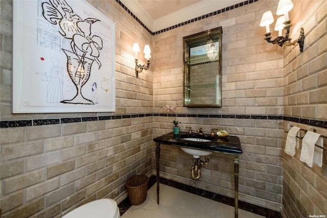 bathroom featuring toilet, sink, brick wall, and ornamental molding