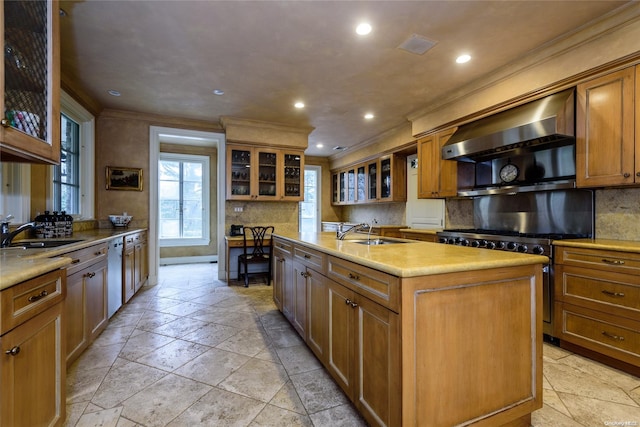 kitchen featuring a kitchen island with sink, sink, crown molding, wall chimney exhaust hood, and high end stove