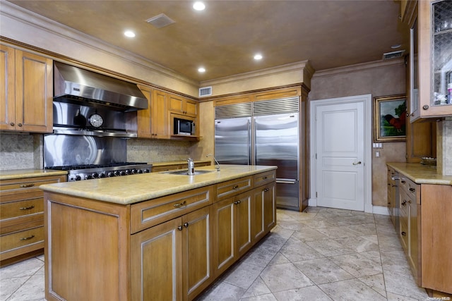 kitchen featuring stainless steel appliances, crown molding, wall chimney range hood, sink, and an island with sink