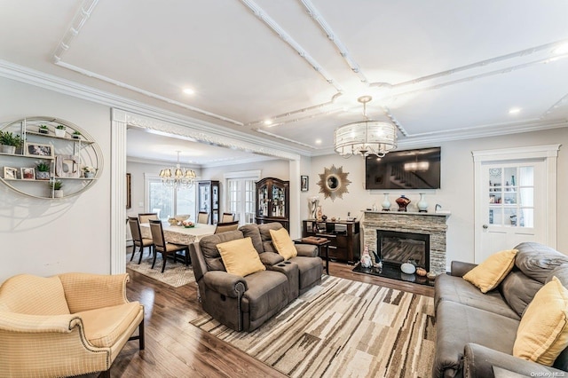 living room with hardwood / wood-style floors, a stone fireplace, crown molding, and an inviting chandelier