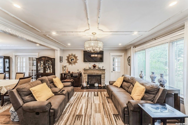 living room with hardwood / wood-style flooring, a stone fireplace, ornamental molding, and an inviting chandelier