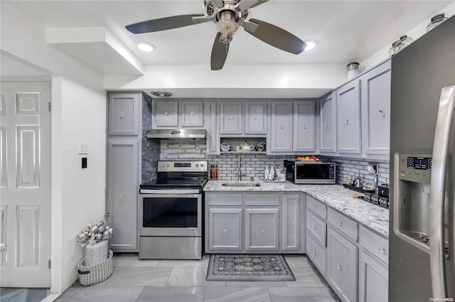 kitchen featuring sink, light stone counters, gray cabinets, decorative backsplash, and appliances with stainless steel finishes