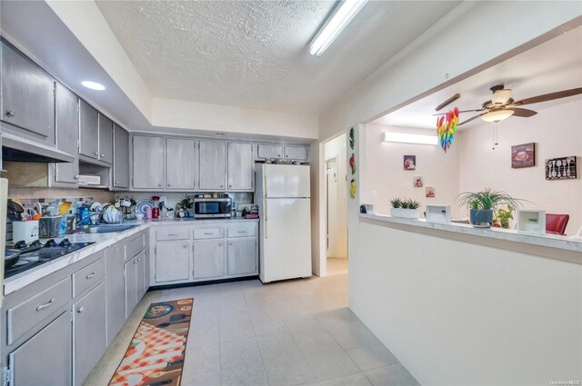 kitchen with gray cabinetry, white fridge, black gas stovetop, and a textured ceiling