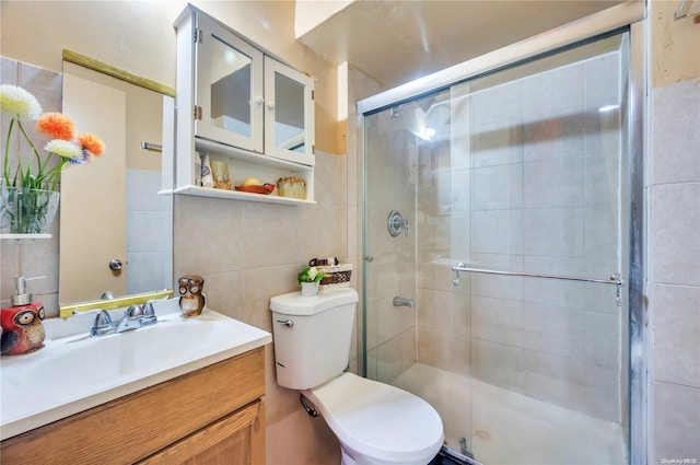 bathroom with vanity, toilet, a shower with shower door, and tile walls