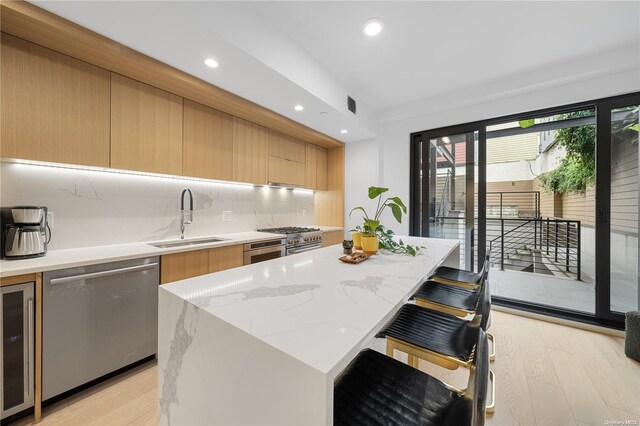 kitchen featuring sink, a center island, light hardwood / wood-style flooring, a breakfast bar, and appliances with stainless steel finishes