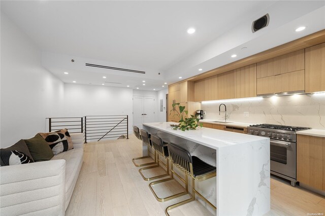 kitchen with stainless steel stove, backsplash, a breakfast bar area, a kitchen island, and light wood-type flooring