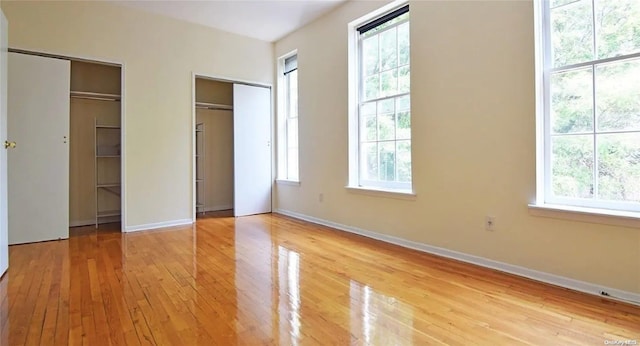 unfurnished bedroom featuring two closets, light hardwood / wood-style flooring, and multiple windows