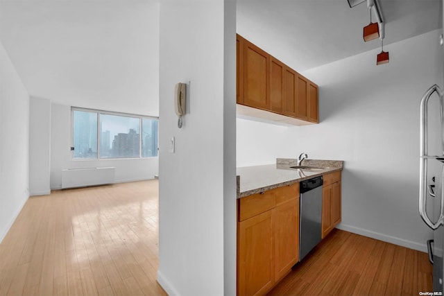 kitchen featuring radiator, sink, light stone counters, stainless steel dishwasher, and light wood-type flooring