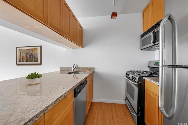 kitchen with light stone counters, sink, stainless steel appliances, and light hardwood / wood-style flooring