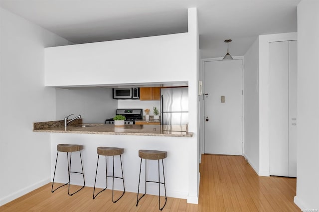 kitchen featuring hanging light fixtures, sink, light wood-type flooring, appliances with stainless steel finishes, and a breakfast bar area