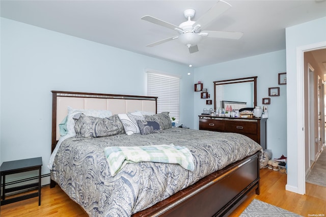 bedroom with light hardwood / wood-style floors, baseboard heating, and ceiling fan