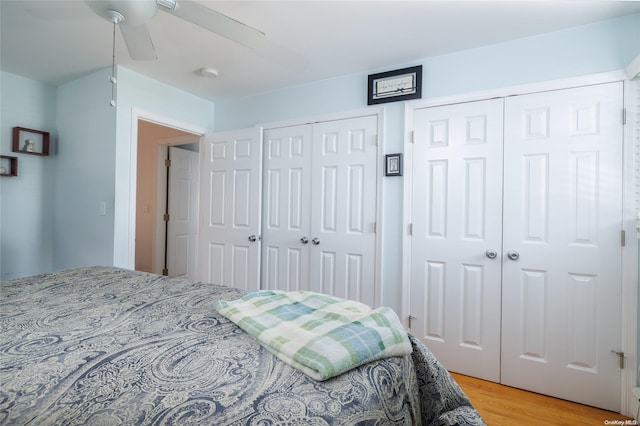 bedroom with hardwood / wood-style flooring, ceiling fan, and two closets