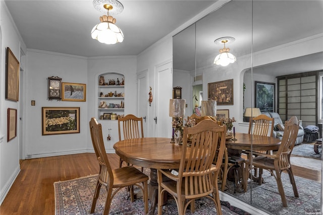 dining space with built in features, wood-type flooring, and ornamental molding