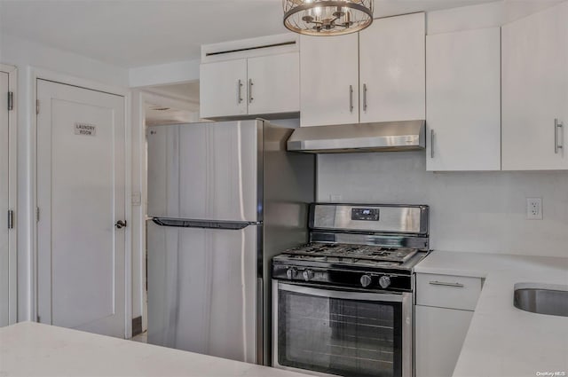 kitchen with appliances with stainless steel finishes, exhaust hood, white cabinets, a chandelier, and hanging light fixtures