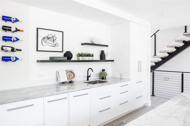 bar with light stone countertops, sink, white cabinets, and light hardwood / wood-style floors