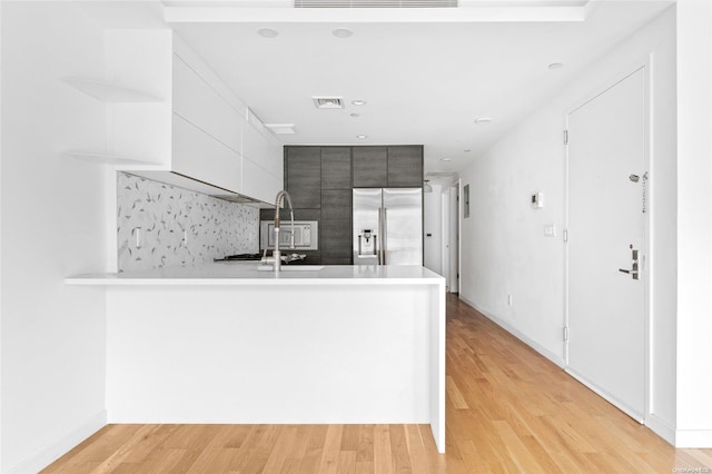 kitchen featuring high end fridge, kitchen peninsula, sink, and light hardwood / wood-style flooring