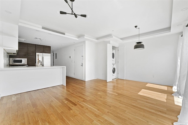 unfurnished living room with stacked washing maching and dryer, light hardwood / wood-style flooring, and a tray ceiling