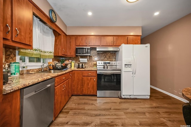 kitchen with tasteful backsplash, wood-type flooring, sink, appliances with stainless steel finishes, and light stone countertops