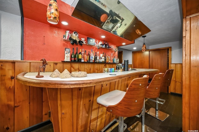 bar featuring wood-type flooring, decorative light fixtures, and wood walls