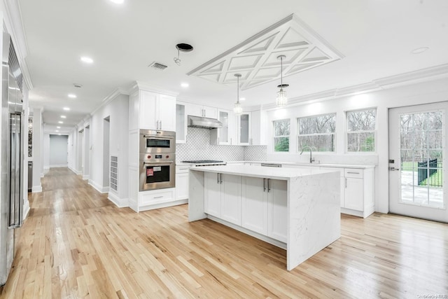 kitchen with light wood-type flooring, ornamental molding, decorative light fixtures, a center island, and white cabinetry