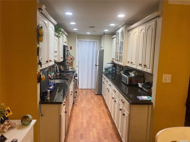 kitchen with appliances with stainless steel finishes, light hardwood / wood-style floors, dark stone countertops, and sink