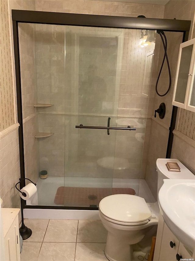 bathroom featuring tile patterned floors, an enclosed shower, toilet, vanity, and tile walls