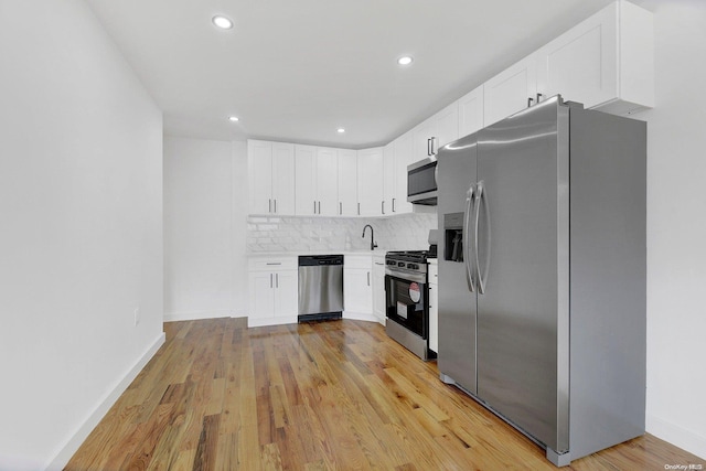 kitchen featuring white cabinets, light wood-type flooring, stainless steel appliances, and backsplash