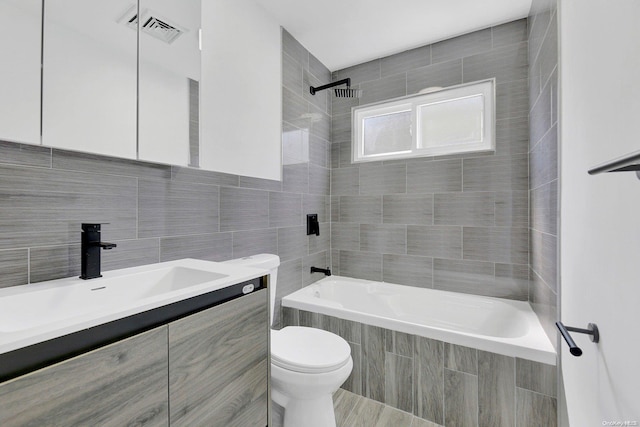 full bathroom with vanity, toilet, tiled shower / bath, and tile walls