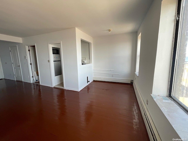 empty room with dark hardwood / wood-style floors and a baseboard heating unit