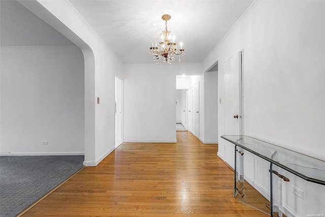 hall with light wood-type flooring, ornamental molding, and a chandelier