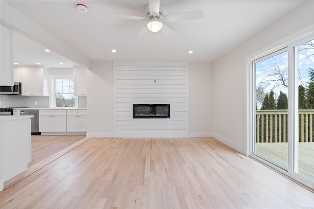 unfurnished living room with a fireplace, ceiling fan, and light wood-type flooring