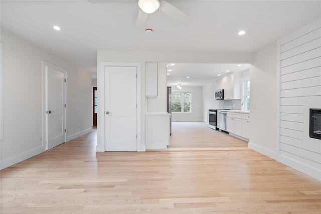 unfurnished living room featuring ceiling fan, a large fireplace, and light hardwood / wood-style flooring